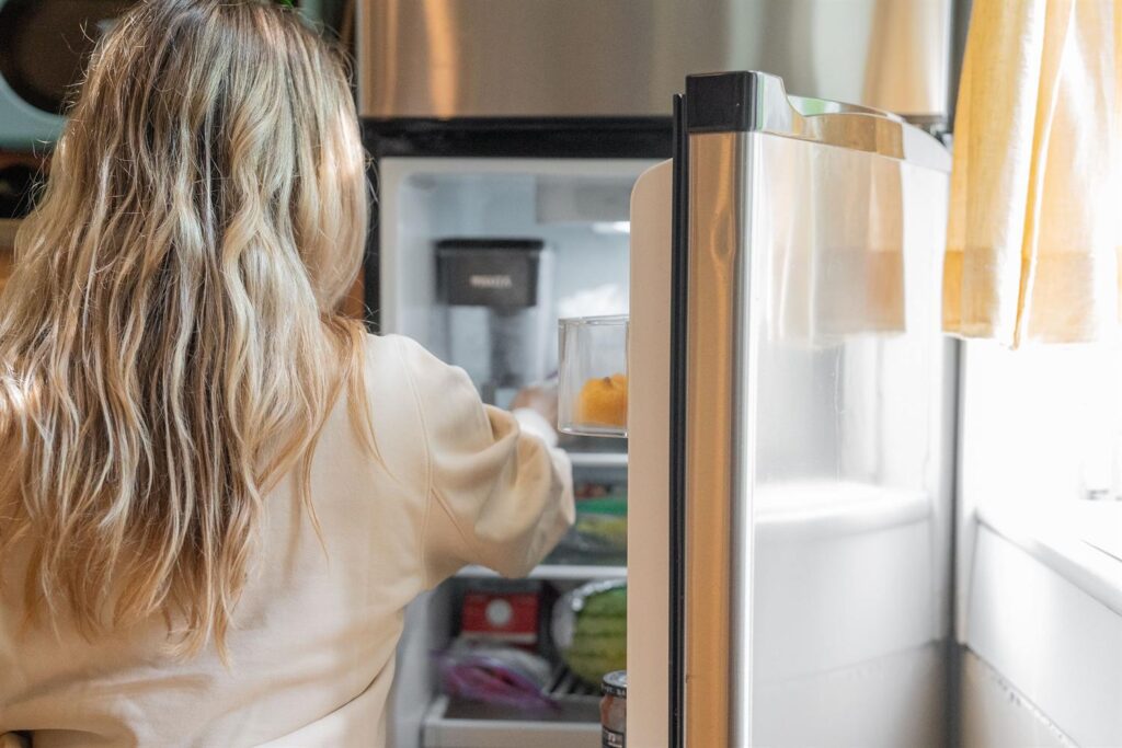 Mulher de costas pegando comida na geladeira em uma cozinha clara