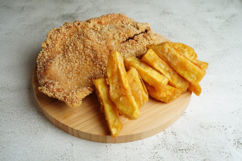 Filé empanado frito e batata frita em tábua de madeira